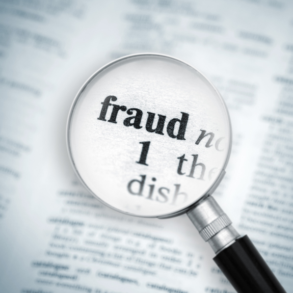 Photo of a magnifying glass hovering of the word Fraud on a page
